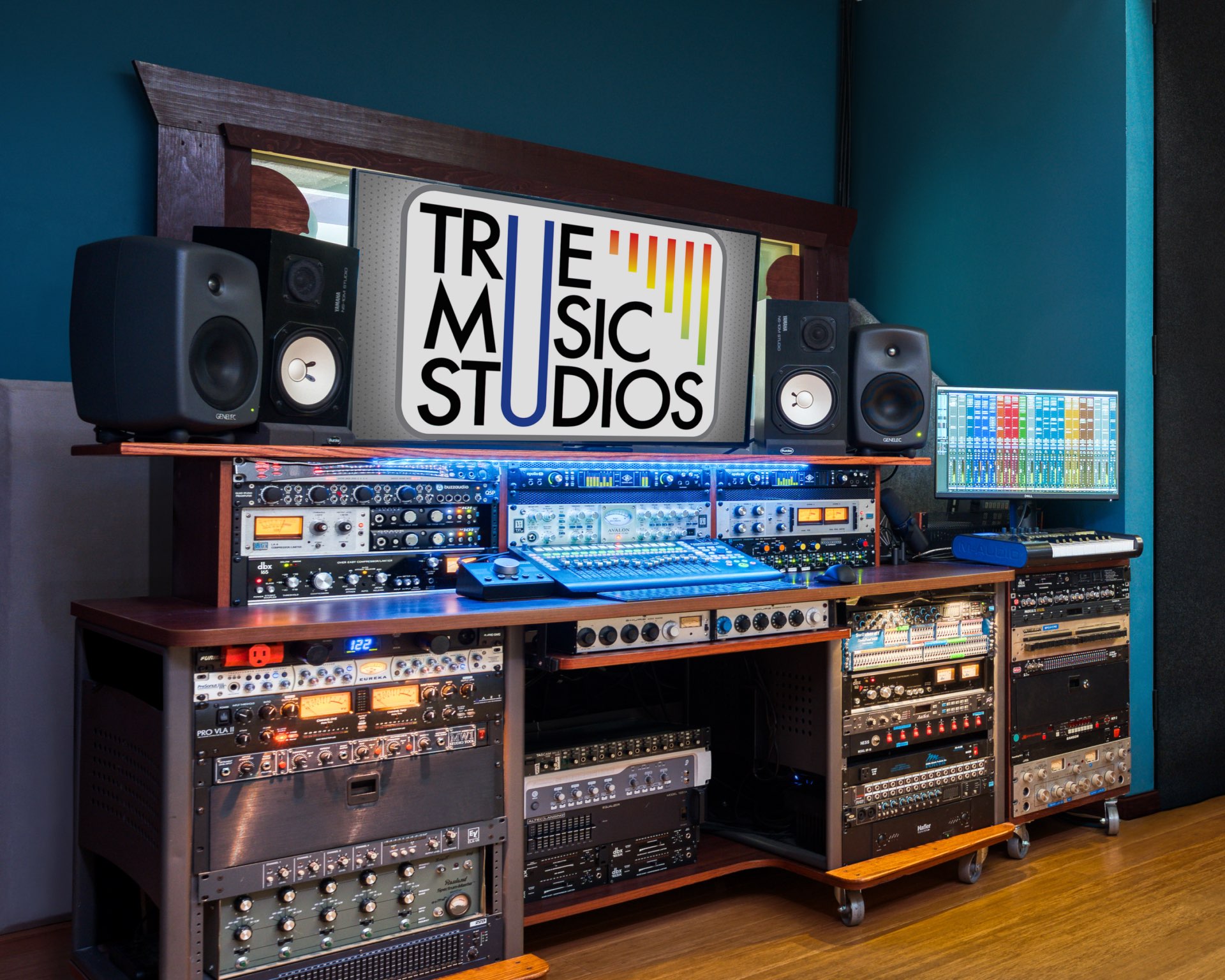 True Music Studios control room with professional audio equipment rack, studio monitors, mixing console, computer screen, and extensive outboard gear collection