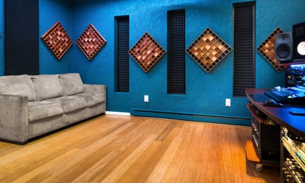 Control room wide view showing desk in front and a couch along the back wall with beautiful wooden panels for acoustic treatment and better sound.
